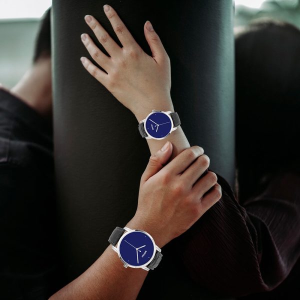 A man and a woman each have a dark blue watch on their hands and are leaning against a wall.