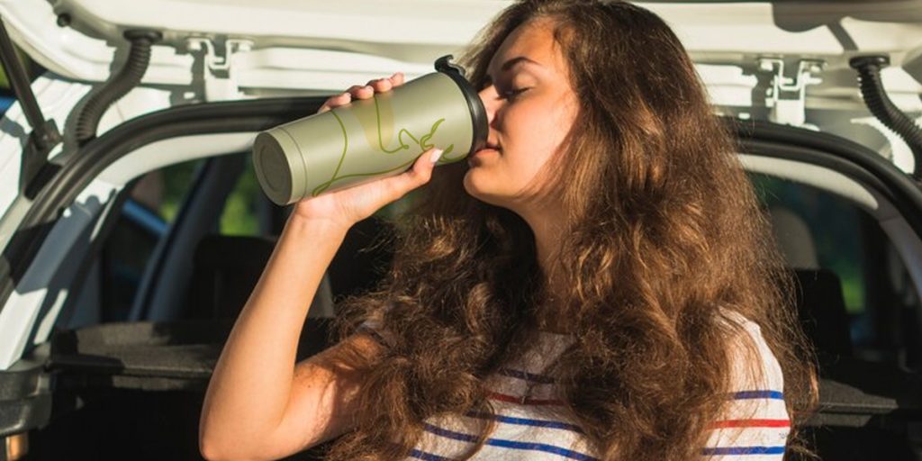 A girl is drinking water from a green thermos