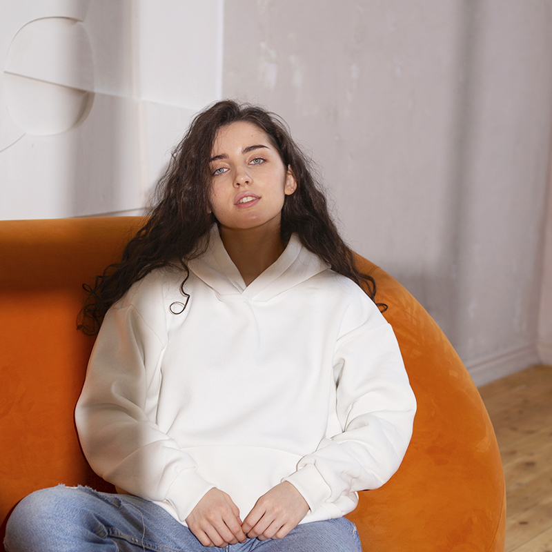 Design Your Own Hoodie A female model in a white hoodie sits on a sofa