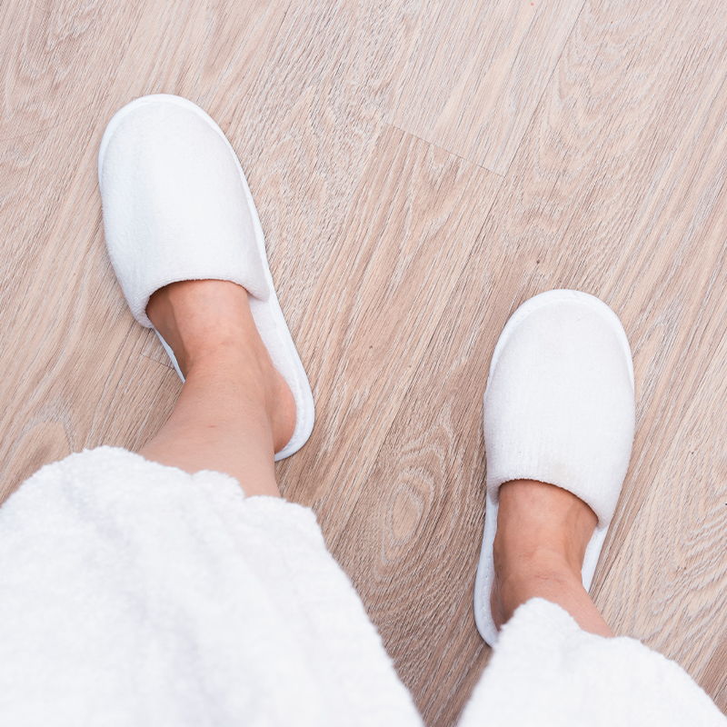 Pure white customizable slippers A person is walking on a wooden floor wearing a pair of pure white slippers